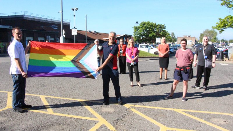 A group of staff stand outside the University Hospital of North Tees. Two of them hold the LGBTQ+ Pride flag.