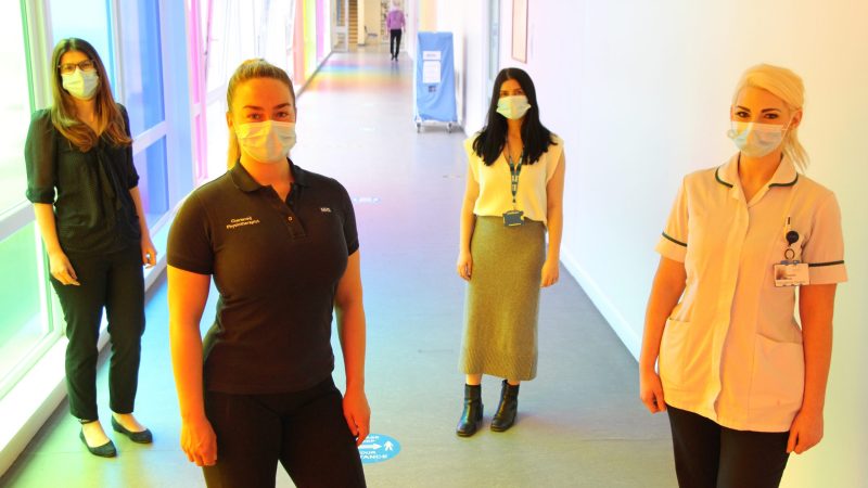 The therapy team stand in a corridor. They wear face masks.