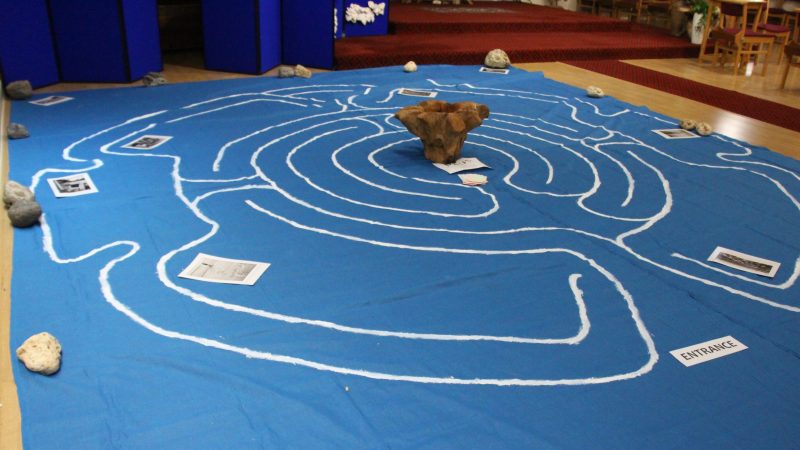A labyrinth is drawn on a large blue mat on the floor. A wooden bowl is in the centre.