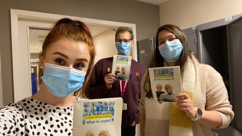 Medical students hold a leaflet. It reads: "Covid-19 vaccination: What to expect".