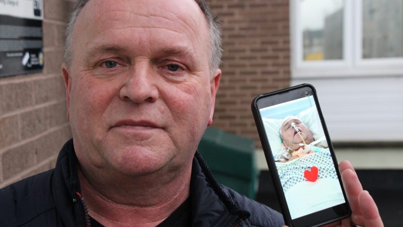 Anthony Seery. He holds up his phone showing a photo of himself in a coma.