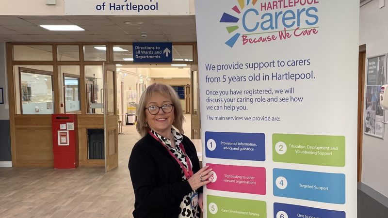 Sharon stands in front of a banner. The banner reads: "Hartlepool Carers: Because we care. We provide support to carers from 5 years old in Hartlepool."