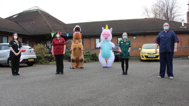 Care home staff. One is dressed as a dinosaur and one is dressed as a unicorn.