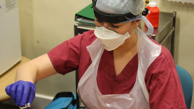 A member of staff prepares a Covid vaccine. She wears PPE.