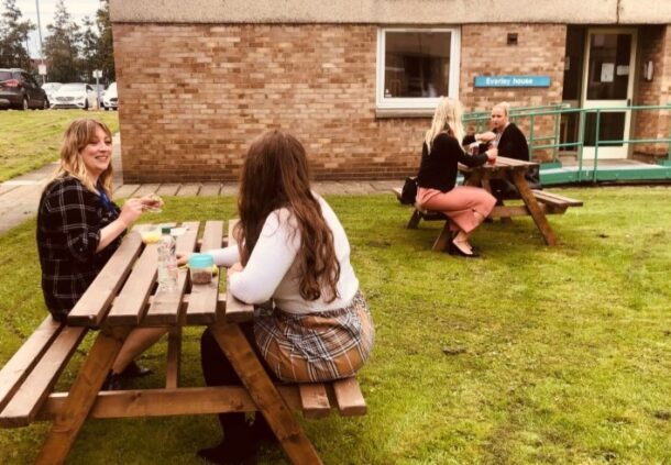 Staff sit at picnic benches.