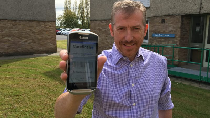 Tony Naylor holds a CareScan+ device. The screen shows a barcode.